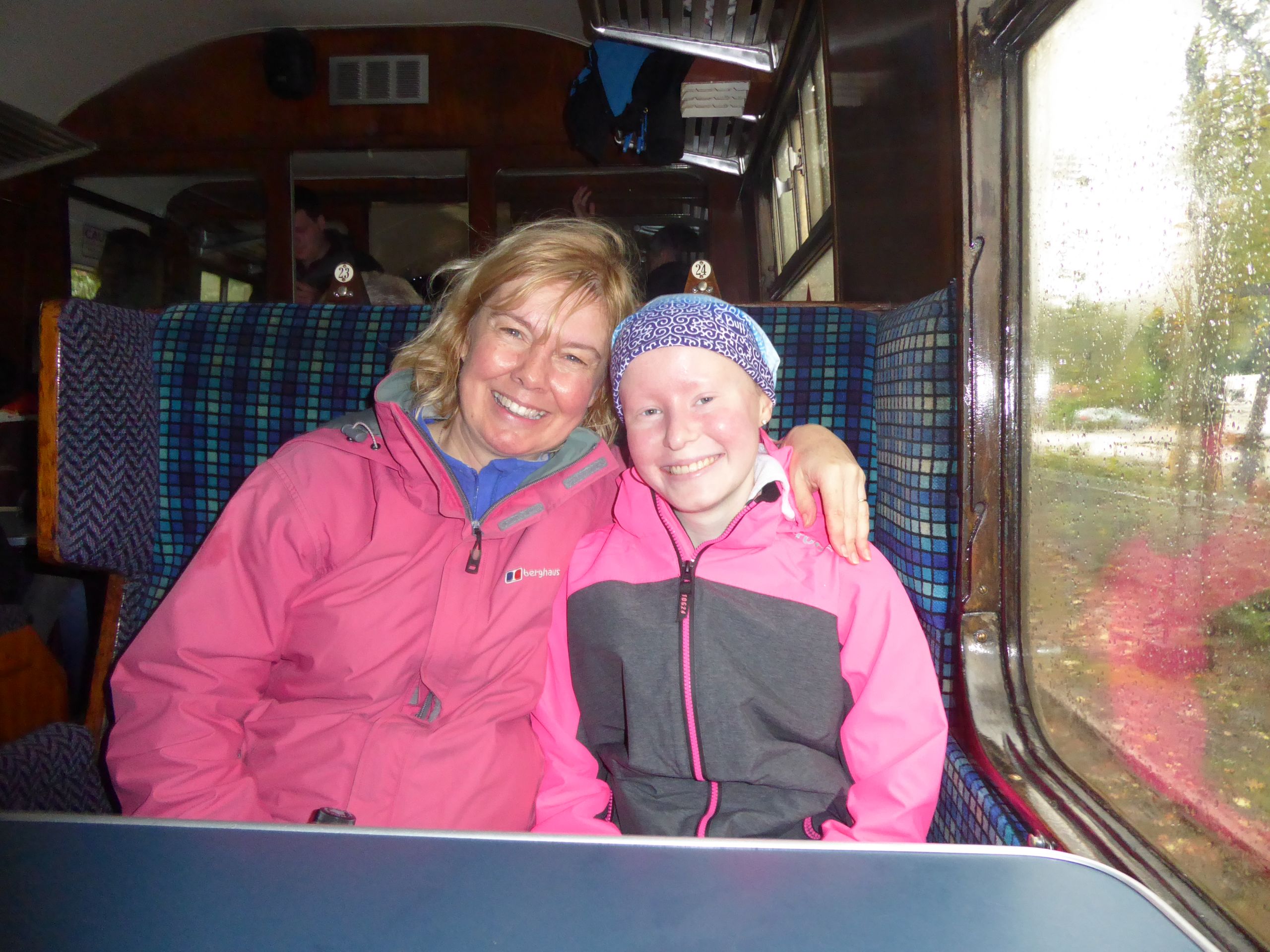 Mum Anita and her daughter Jess on a train going to Lake District. Wearing pink jackets. Jess has a headscarf on.