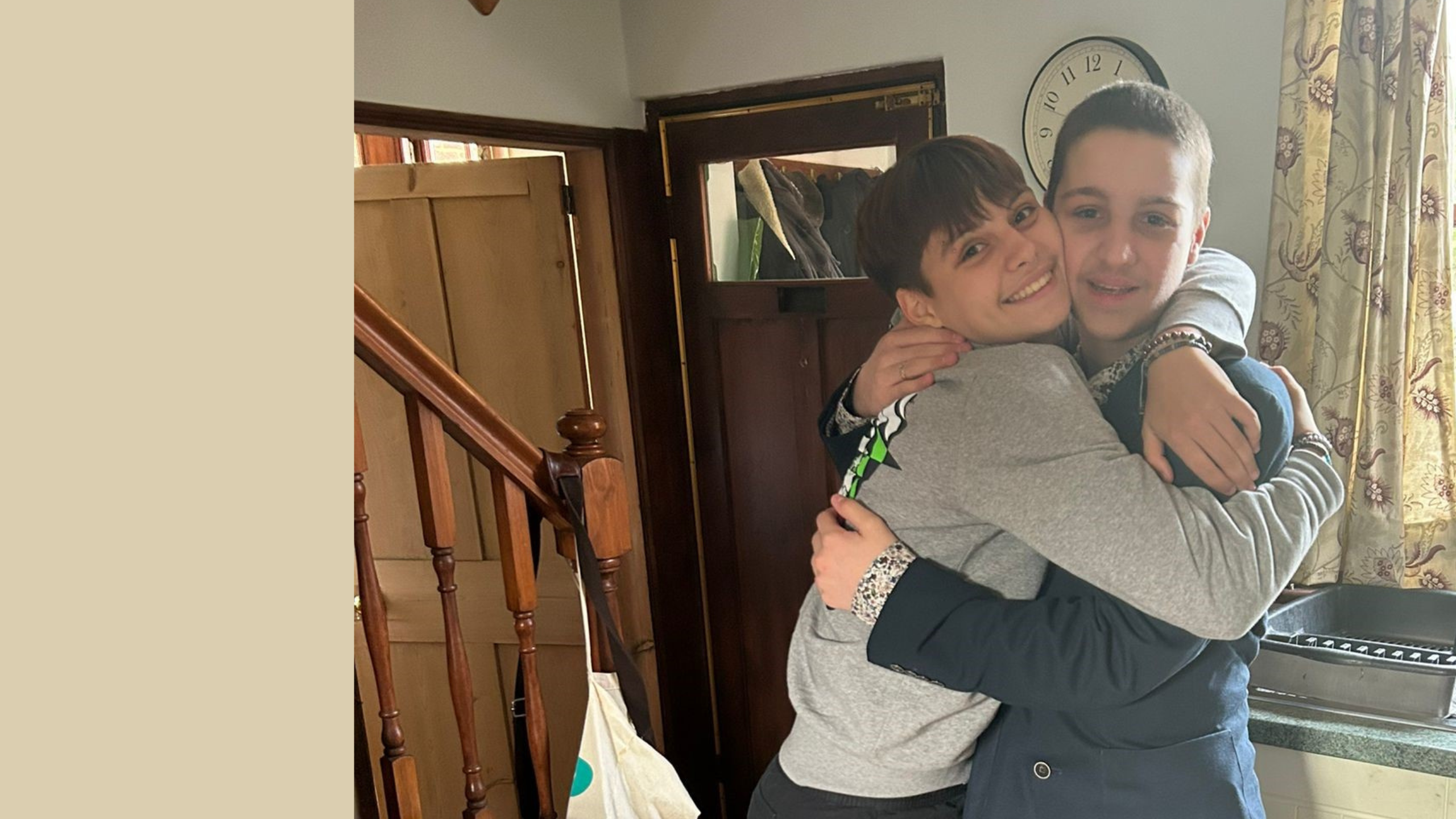 A brother and a sister hugging each other tightly, while looking at the camera. The boy on the right has very short brown hair and a navy jacket. The girl on the left has short brown hair and is wearing a grey sweatshirt. They are both smiling.