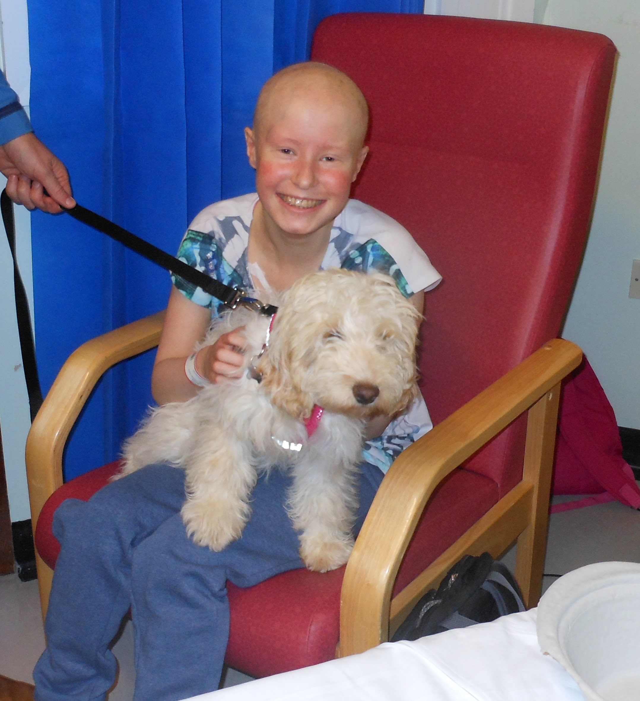 Jess, with a big smile, hugging her puppy who is now quite big and shaggy. Jess's hair has fallen out from having chemotherapy