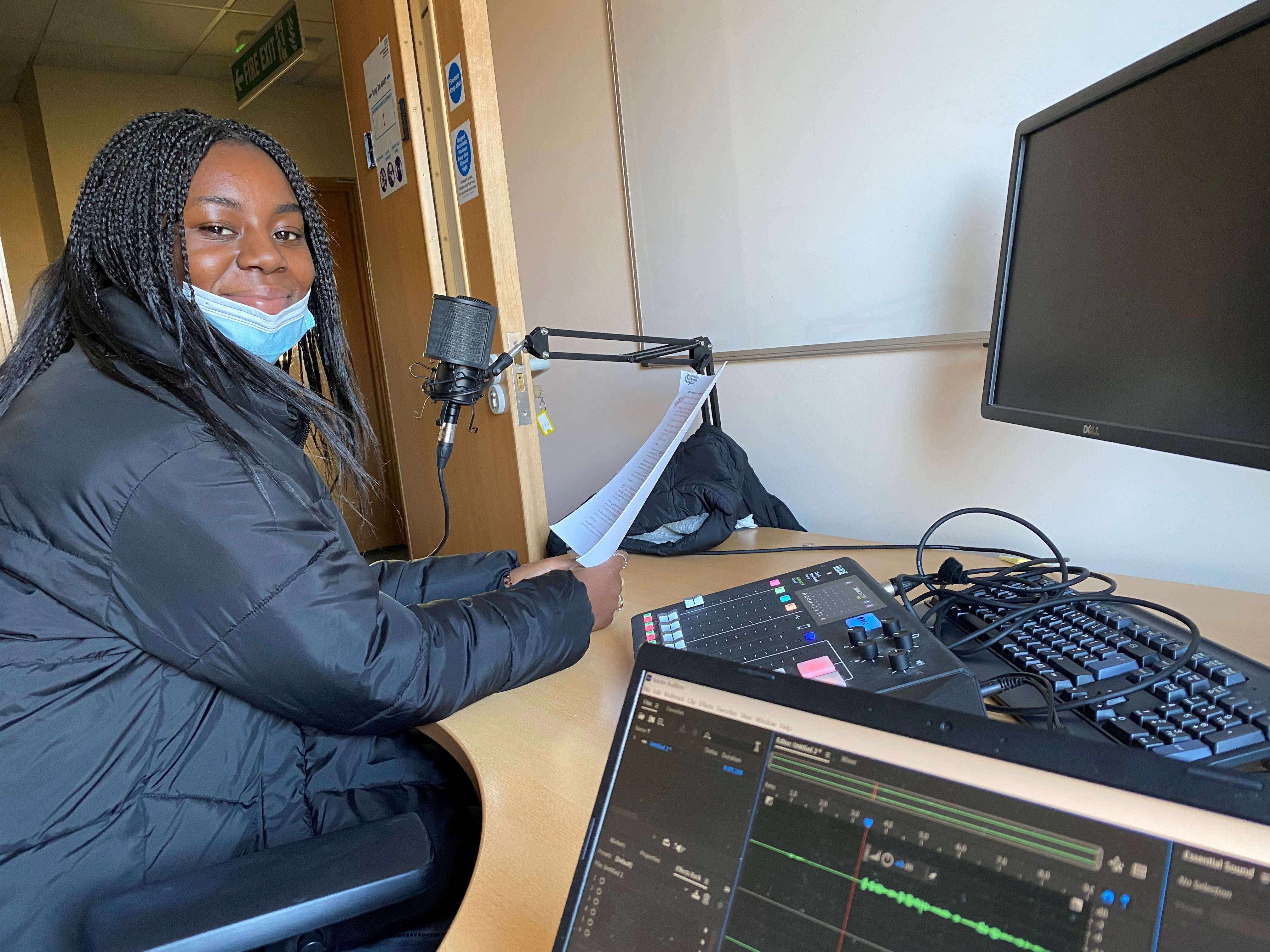 young black girl with long hair sits at desk with script and microphone