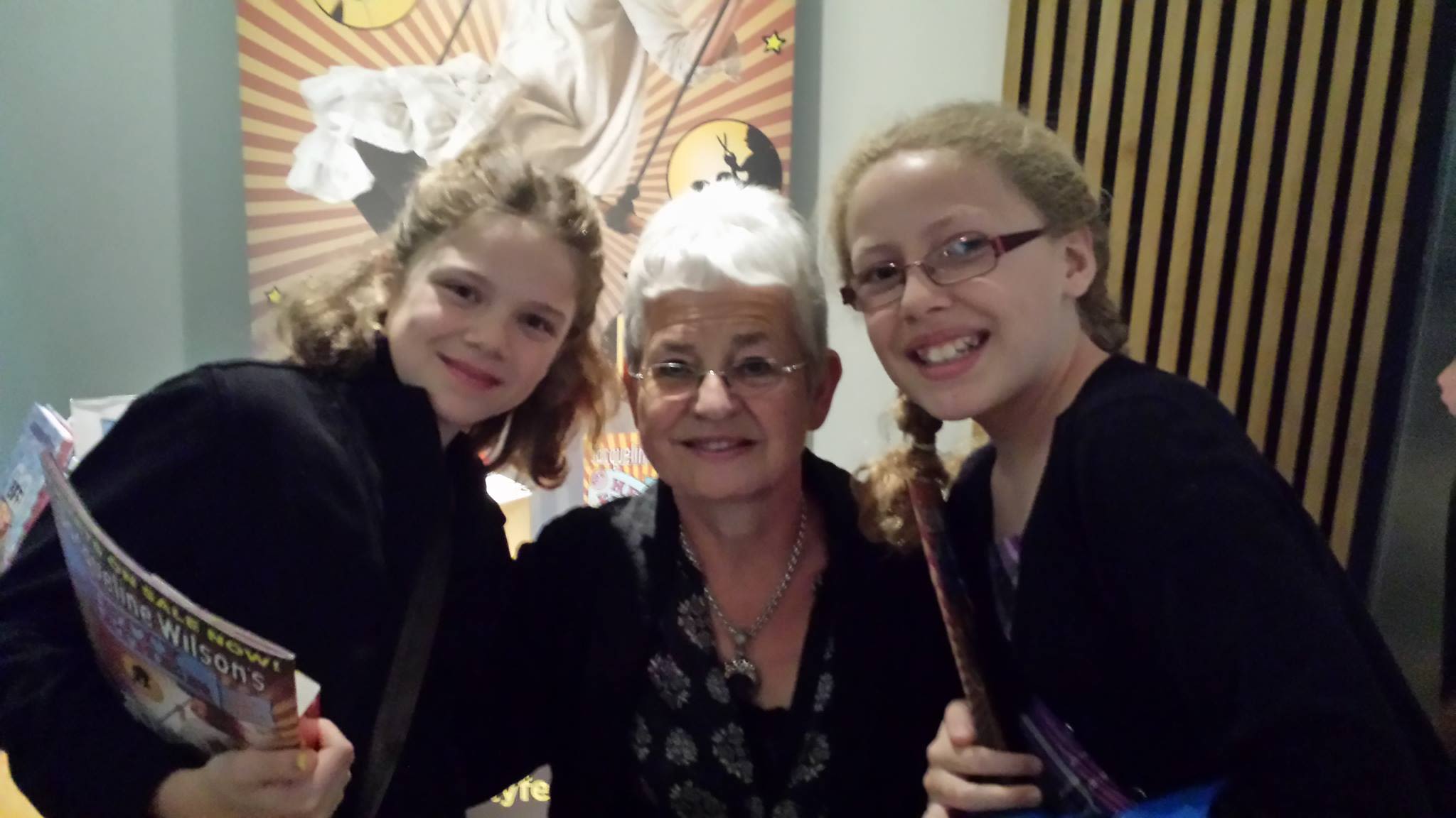 Olina smiling alongside her sister, with author Jacqueline Wilson in the middle