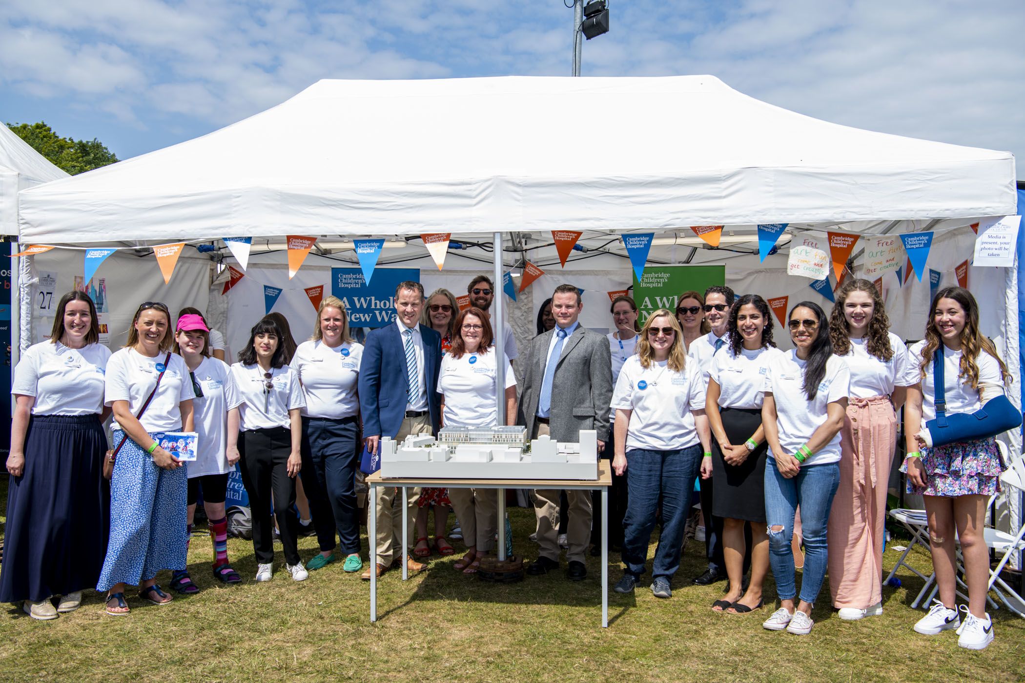 A large group of people from the Cambridge children's hospital project smile for the camera. They are gathered around a model of the new hospital