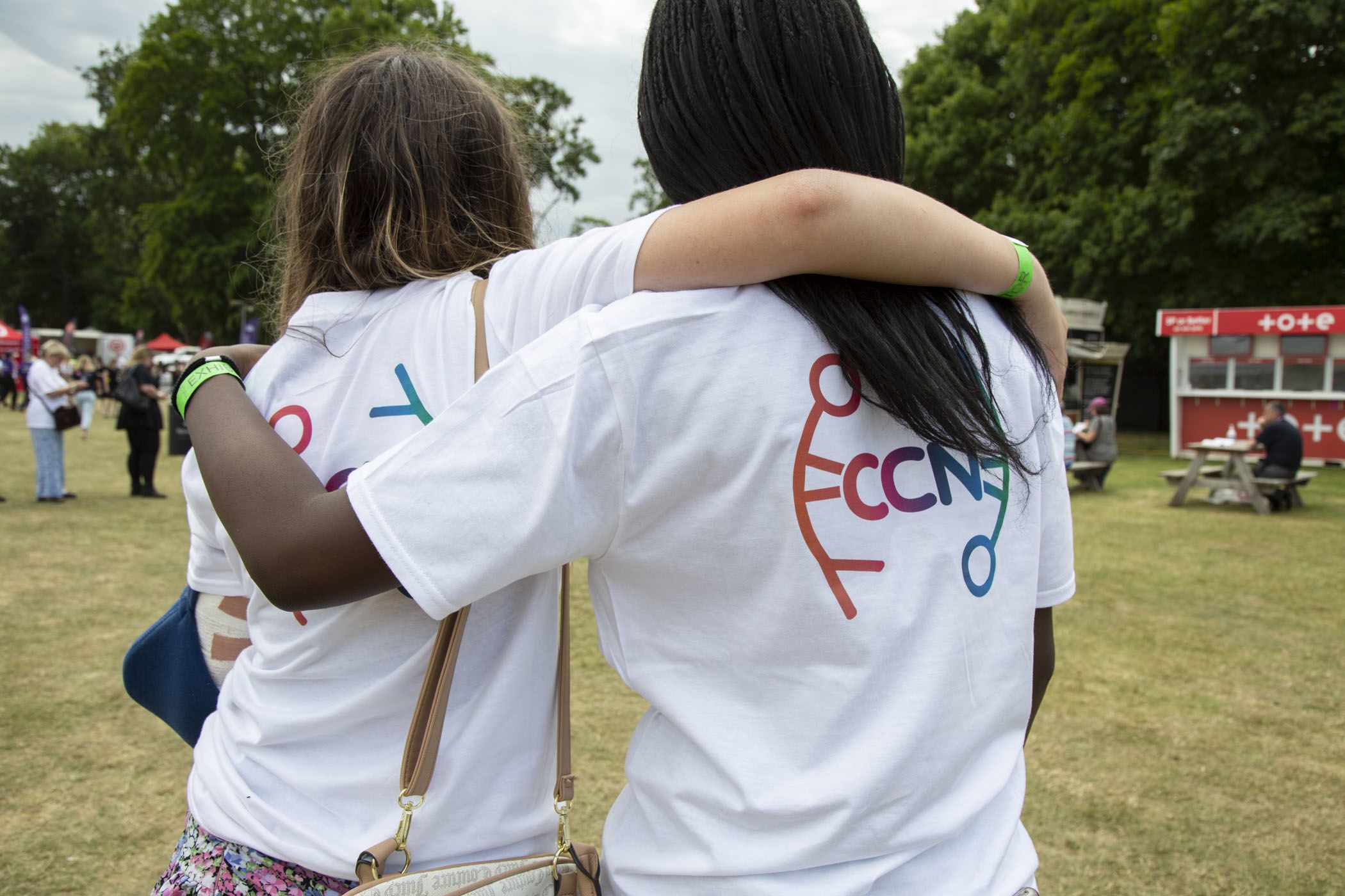Two teenagers have their arms around each other's shoulders, backs to the camera
