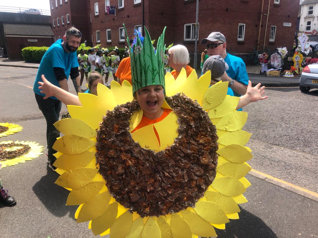 A young girl in a sunflower costume, holding her arms out wide and laughing