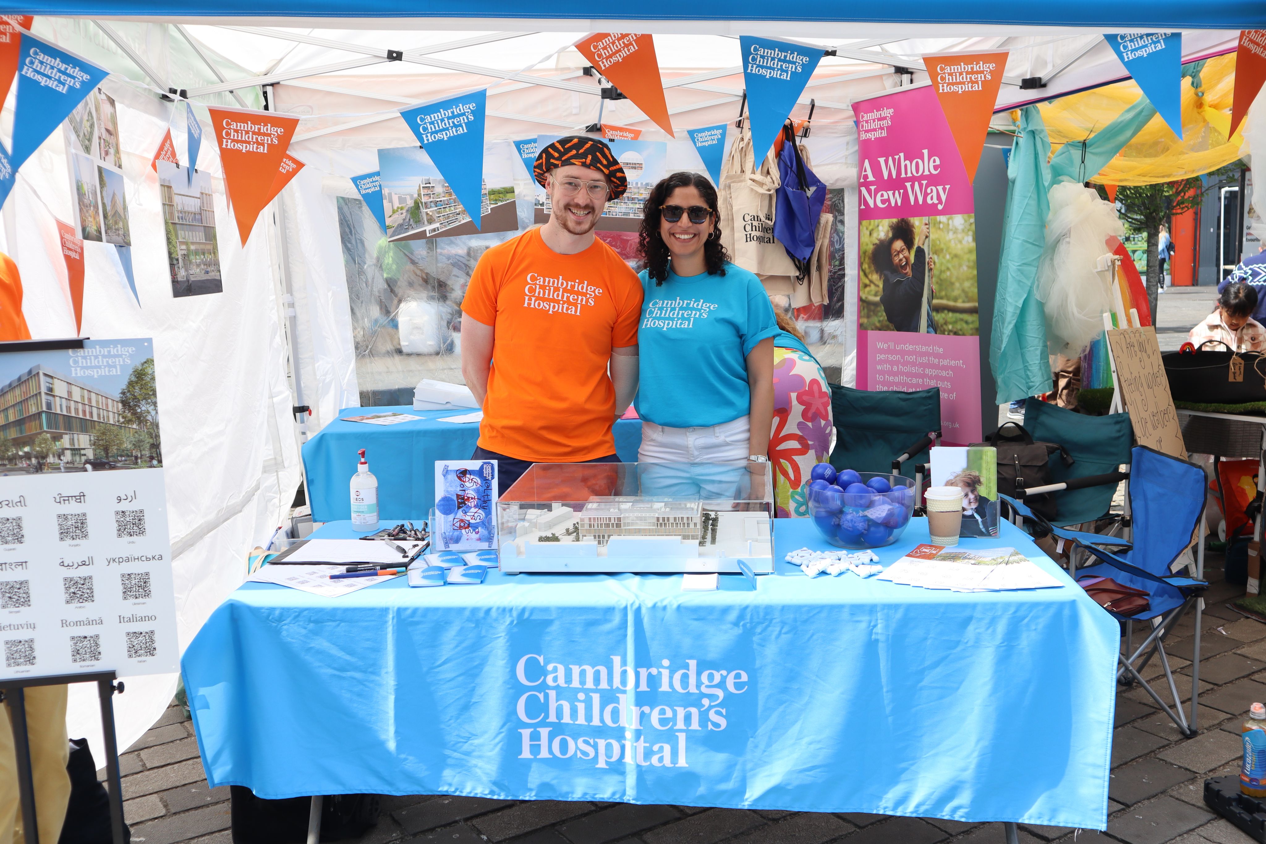 A man in a stripy hat and a woman in sunglasses stand in a marquee with bunting and a decorated table