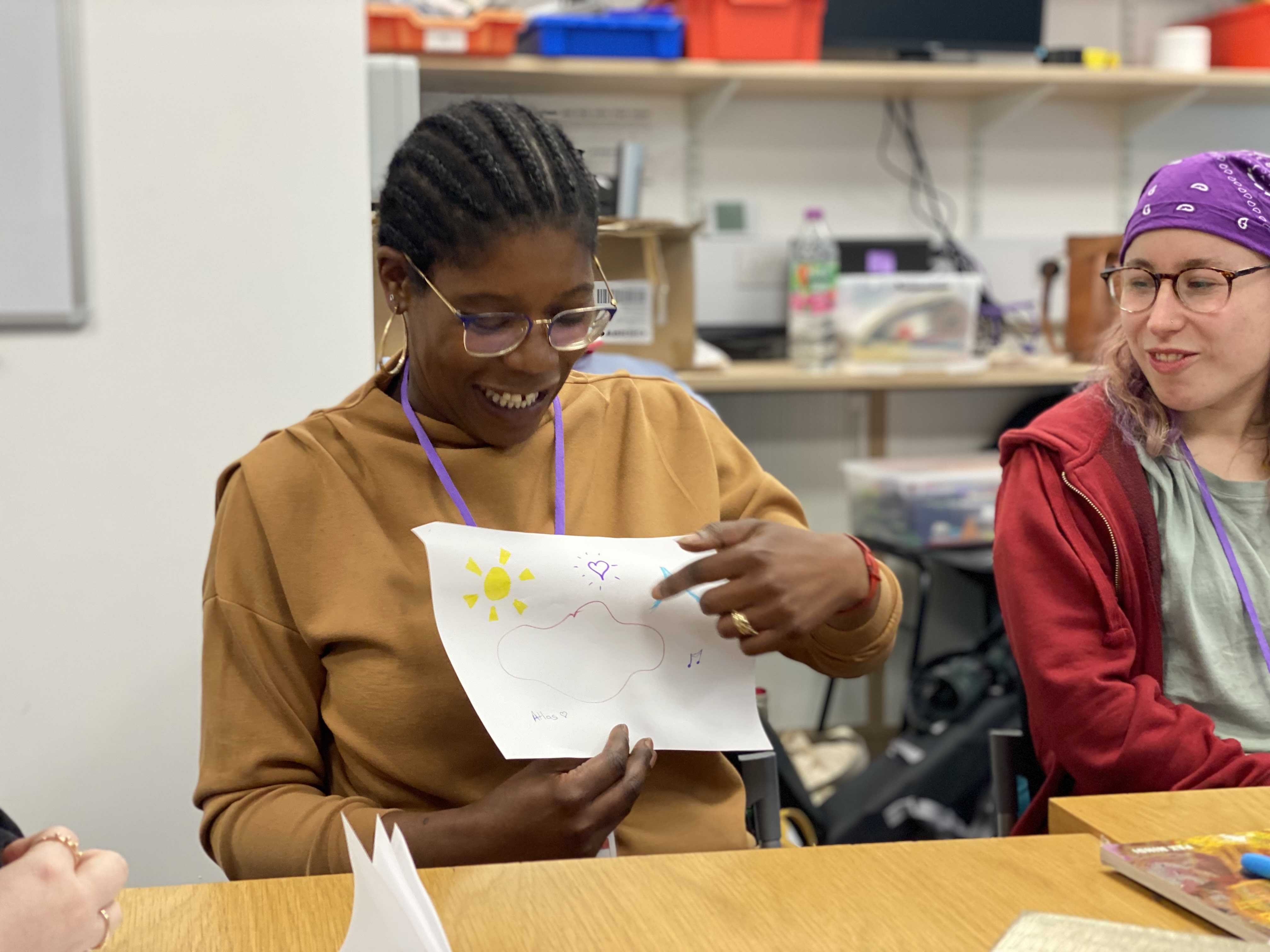 A lady holds up a picture of a sunshine and cloud that she has drawn