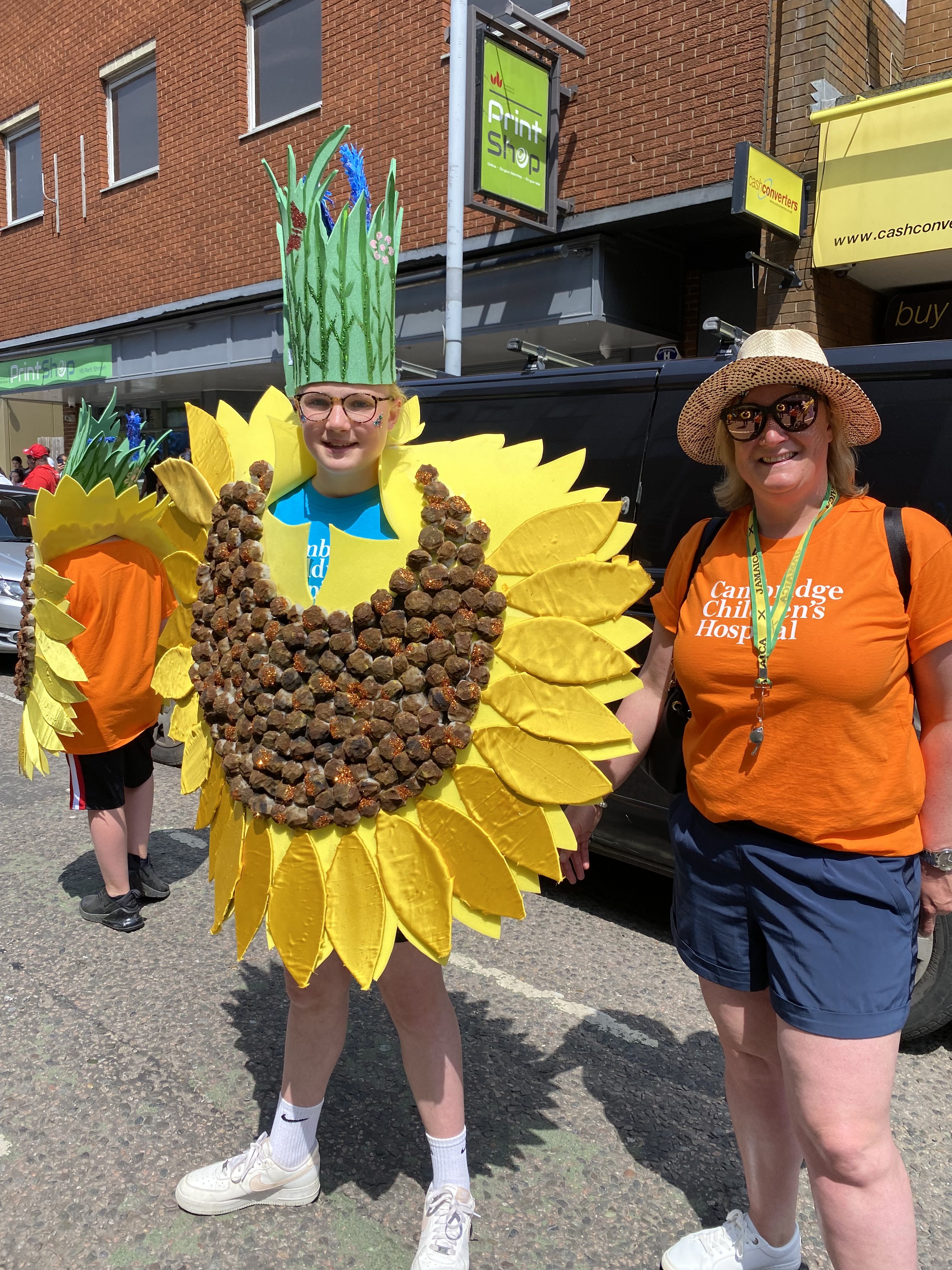 A girl dressed as a sunflower and a lady with a straw hat and sunglasses smiling 