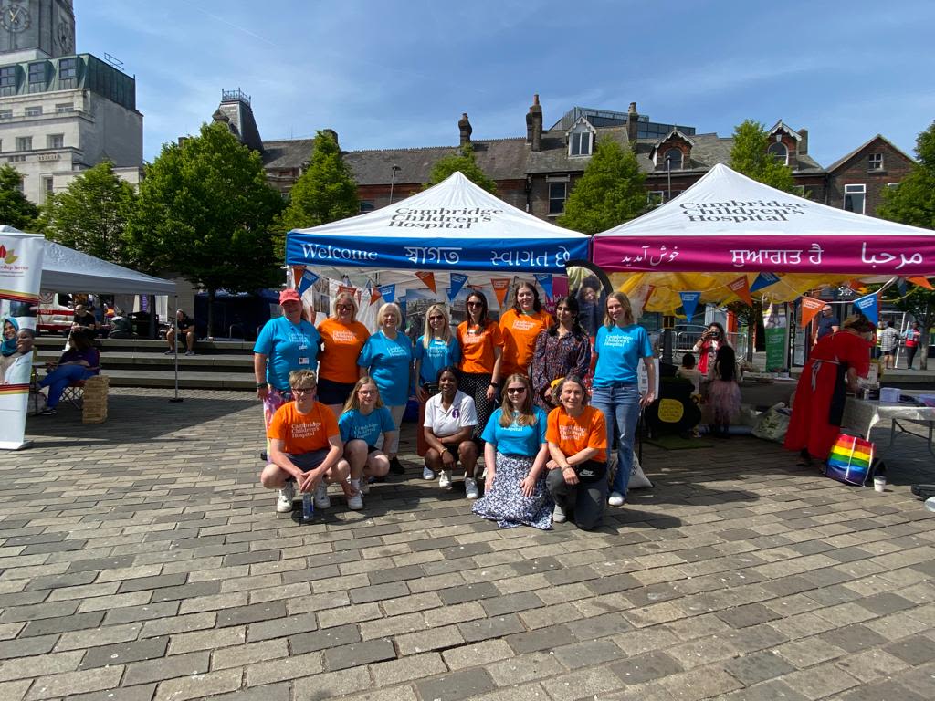 A team of people from Cambridge Children's Hospital posing for the camera beside a white marquee with a blue and pink banner wrapped around it.