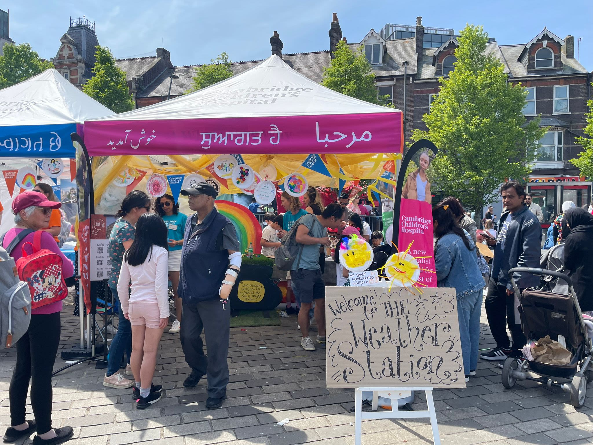People milling about outside a marquee with a pink banner wrapped around in