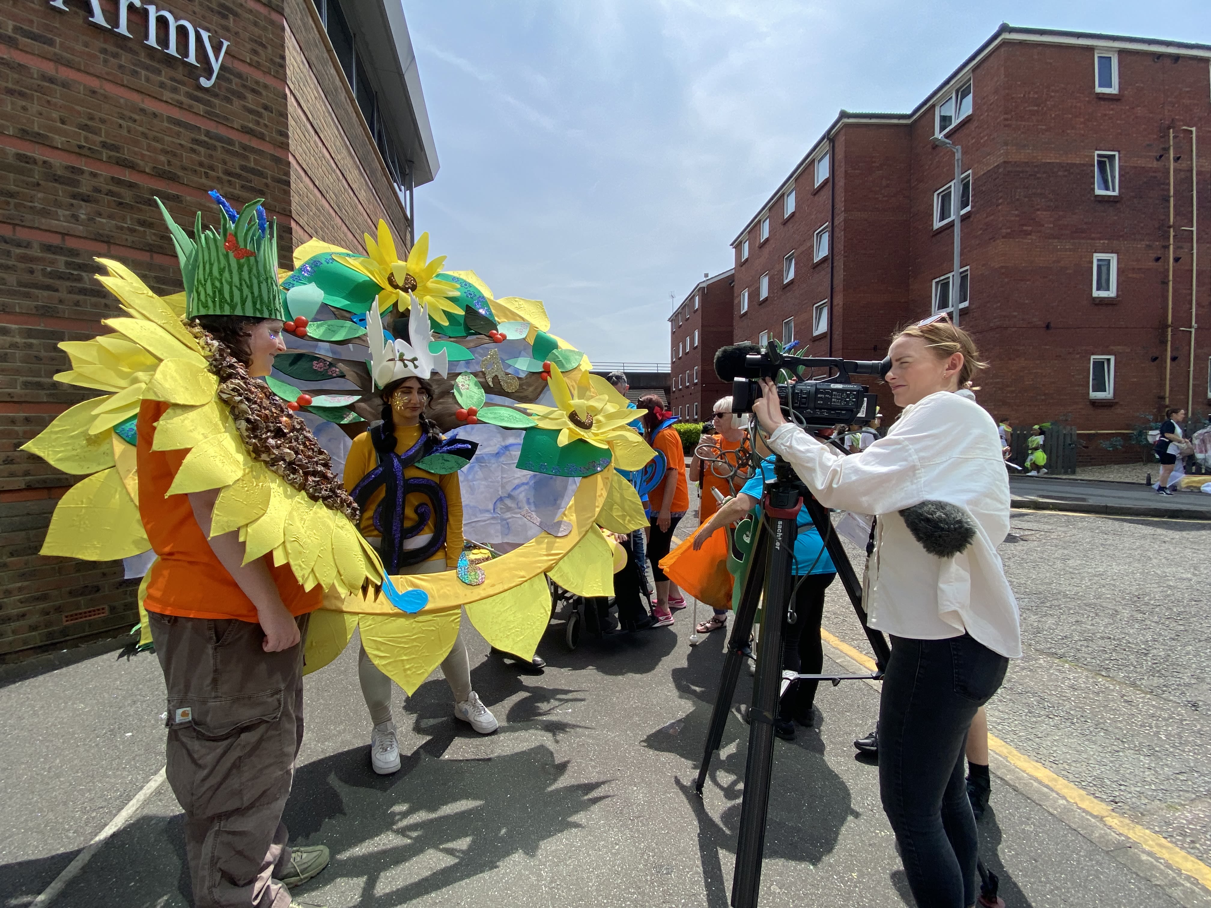 Two teenagers wearing carnival costumes are interviewed by a lady with a camera for the TV