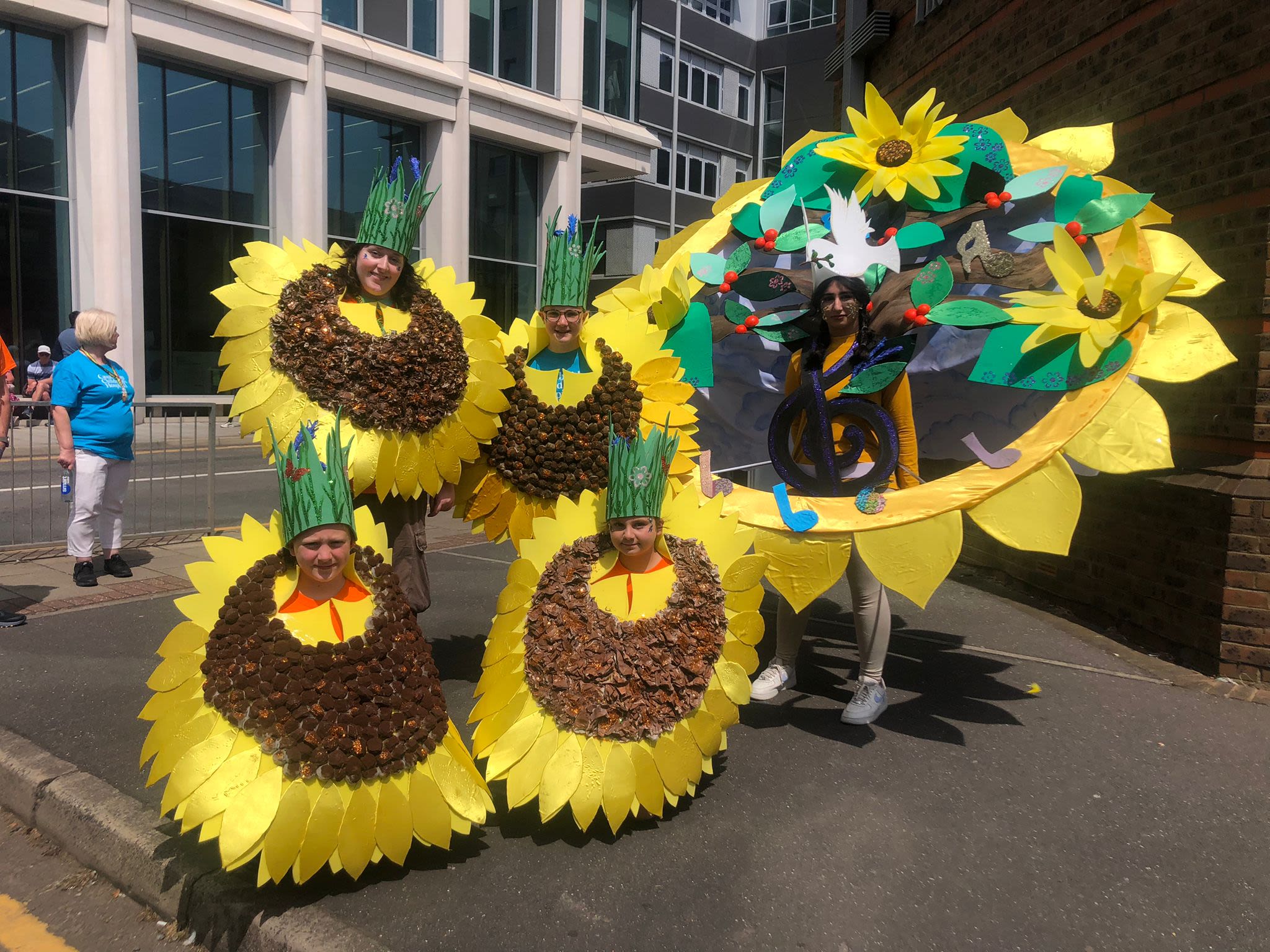 Five young people wearing sunflower carnival costumes. The costumes are very big
