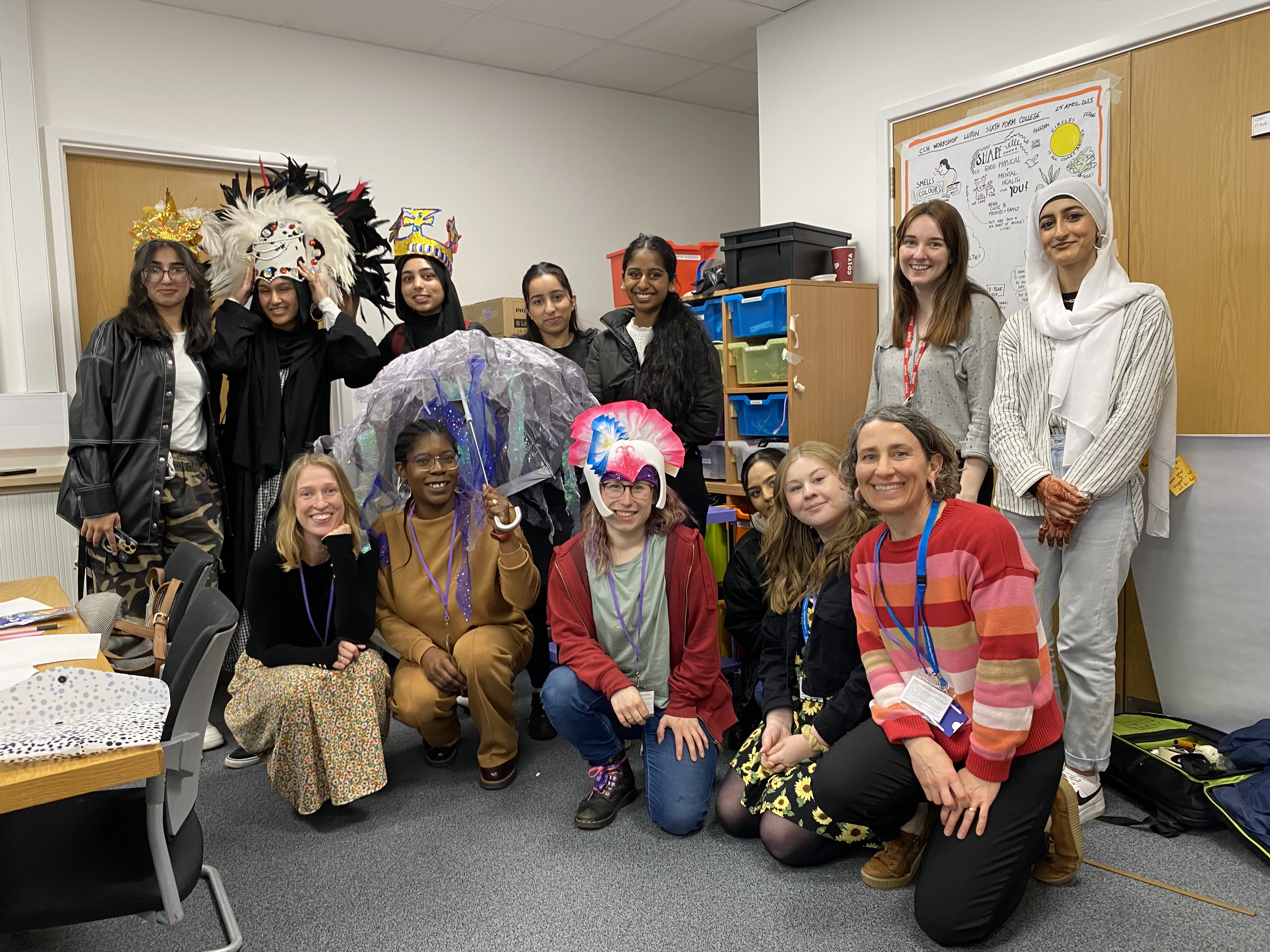 A group of adults and teenagers smiling for the camera. Some are wearing carnival headresses.